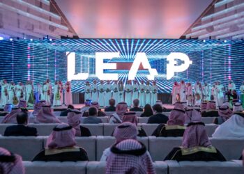 A group of people sit facing a stage with a large "LEAP" sign and performers in traditional attire under vibrant lights.