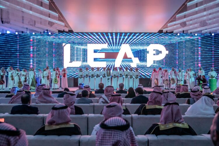 A group of people sit facing a stage with a large "LEAP" sign and performers in traditional attire under vibrant lights.